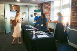 Registration table at an event with staff sorting name badges for attendees, in a room with bookshelves and glass doors in the background.