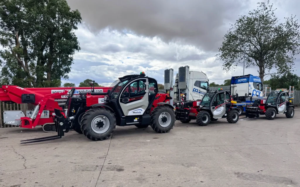 Industrial equipment lot with red telehandlers and white trucks parked in a row under a cloudy sky.
