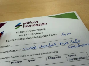 Close-up of a Salford Foundation pamphlet on a wooden desk, showing the logo and a heading that reads 'Kickstart Your Future' with handwritten notes nearby.