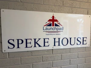 White sign on a brick wall showing the Launchpad logo (red, white, blue) with the word 'Launchpad' and the text 'SPEKE HOUSE' beneath it.