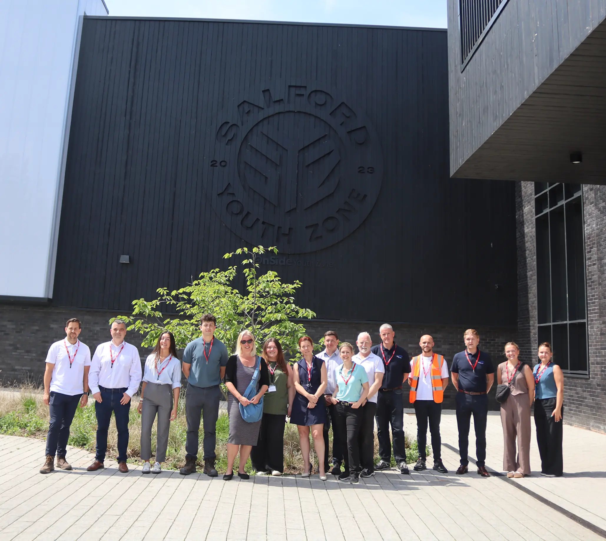 Group of people posing for a photo outside a modern building with a circular emblem on the wall behind them.
