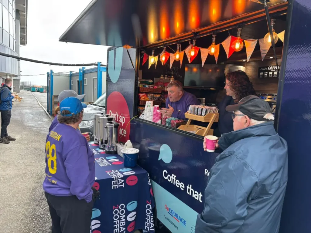 Mobile coffee truck with a service window, two baristas serving customers, and string lights overhead outdoors.