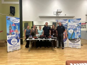 Six staff members stand behind a table at a HireSafe Solutions booth with tall banners and safety posters in a conference hall.