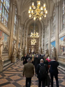 Interior of a Gothic cathedral with ornate chandeliers, tall arches, statues along the walls, and visitors walking down the nave.